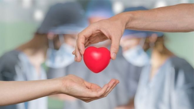 Игрушечное сердце передается из рук в руки на фоне трудящихся в операционной врачей